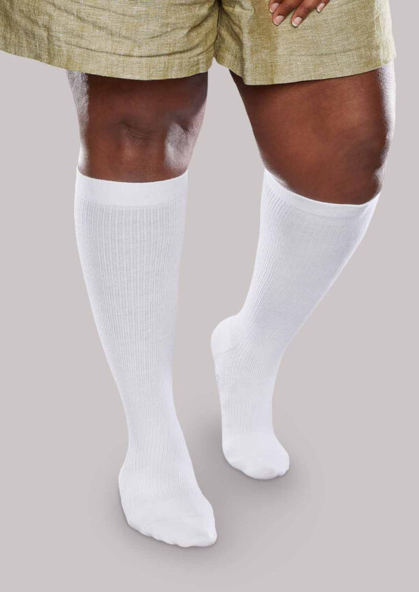 A person wearing Core-Spun 20-30 mmHg knee-length white socks and beige shorts stands with one foot slightly behind the other, facing forward.