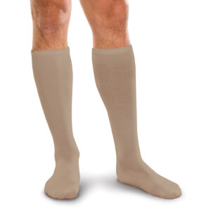 A man is standing on a white background, wearing Core Spun 15-20 mmHg knee-high beige compression socks.