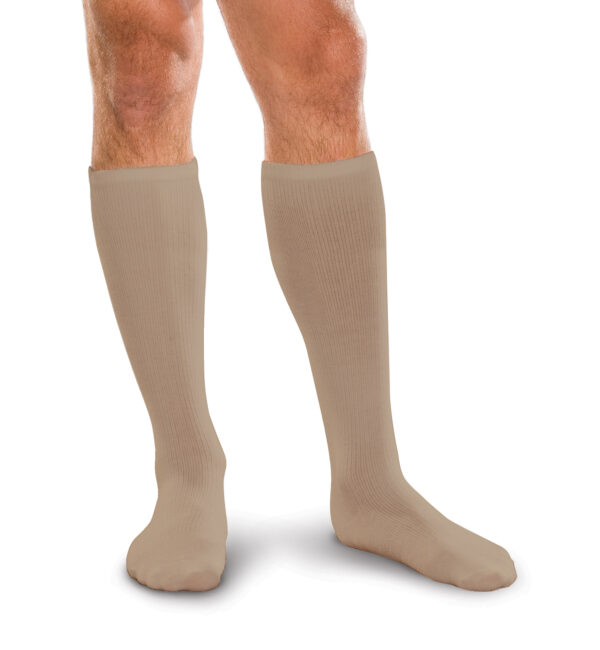 A man is standing on a white background, wearing Core Spun 15-20 mmHg knee-high beige compression socks.