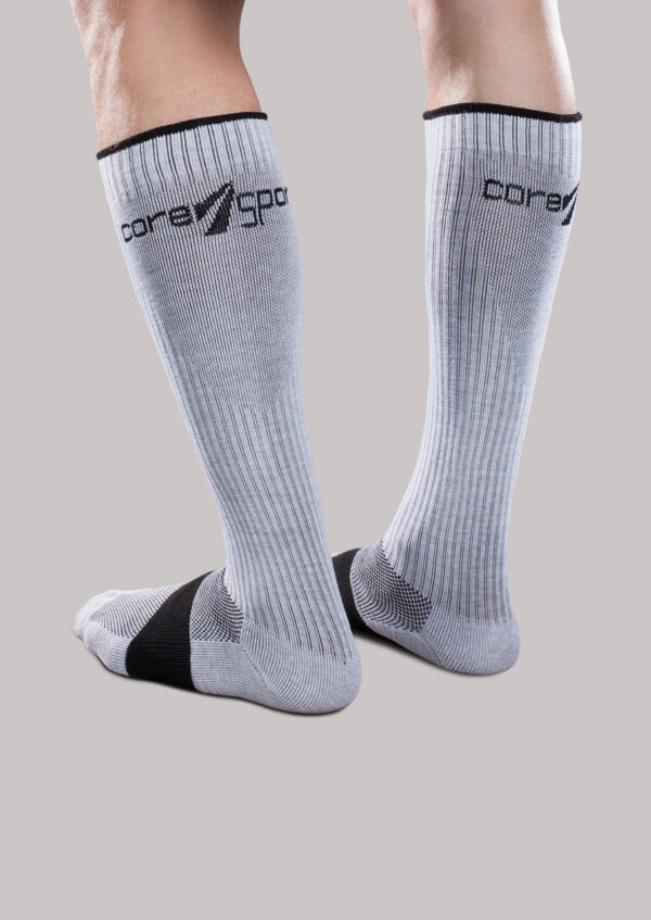 Person wearing gray knee-high socks with black accents and the brand name "Core-Sport by Therafirm" printed near the top.